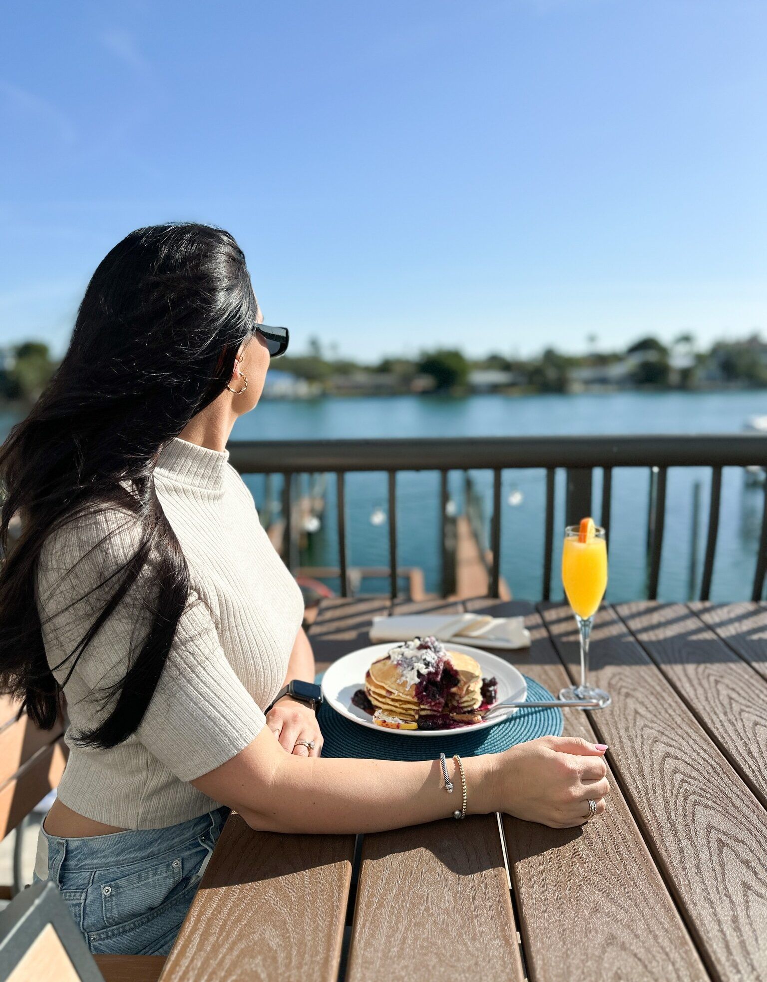 Woman sitting at outdoor table overlooking the water with breakfast plate and drink at Castile Restaurant