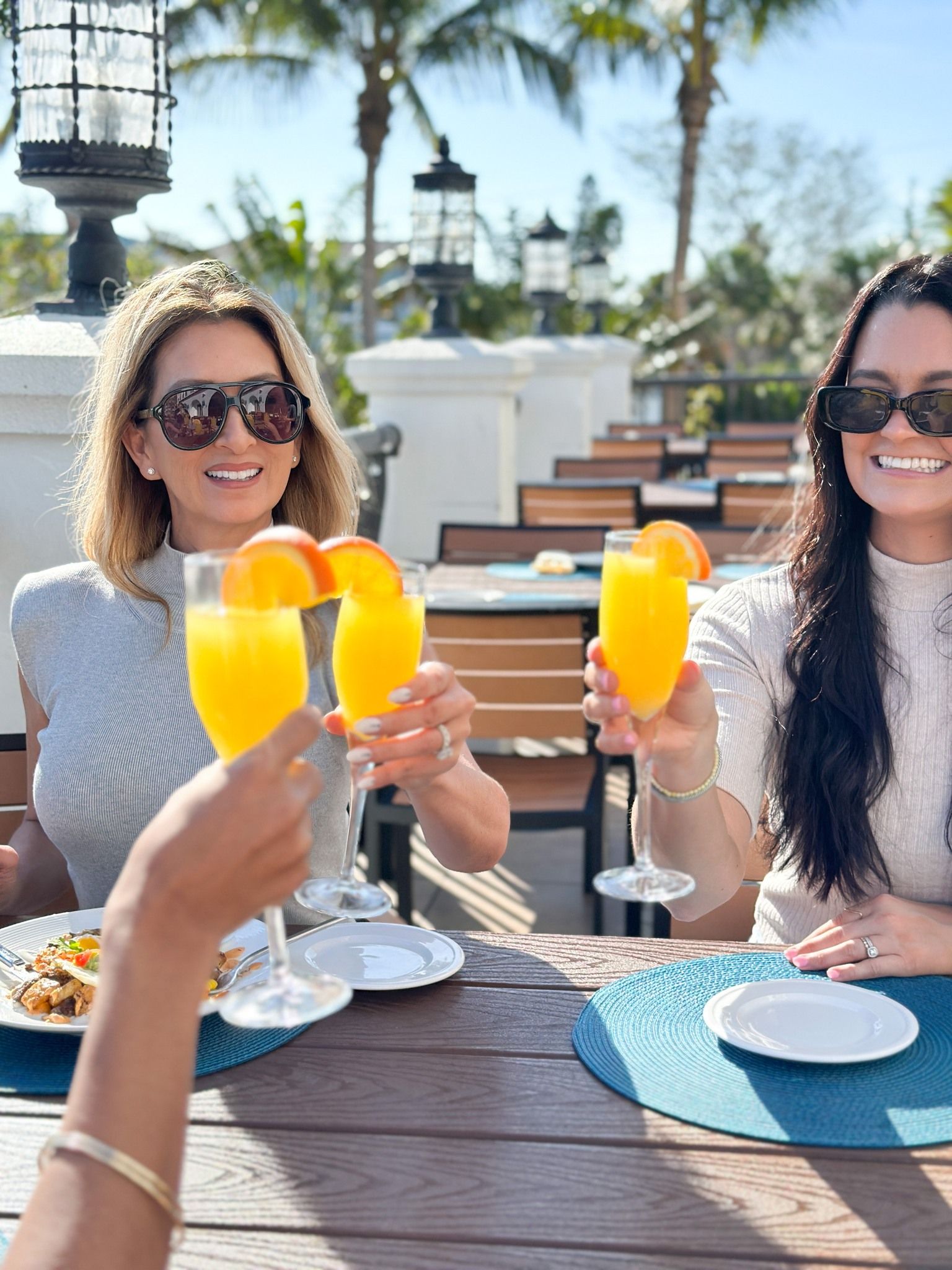 Tres mujeres sentadas en una mesa al aire libre sonriendo y haciendo porras con sus bebidas en el restaurante Castile en St Pete Beach.