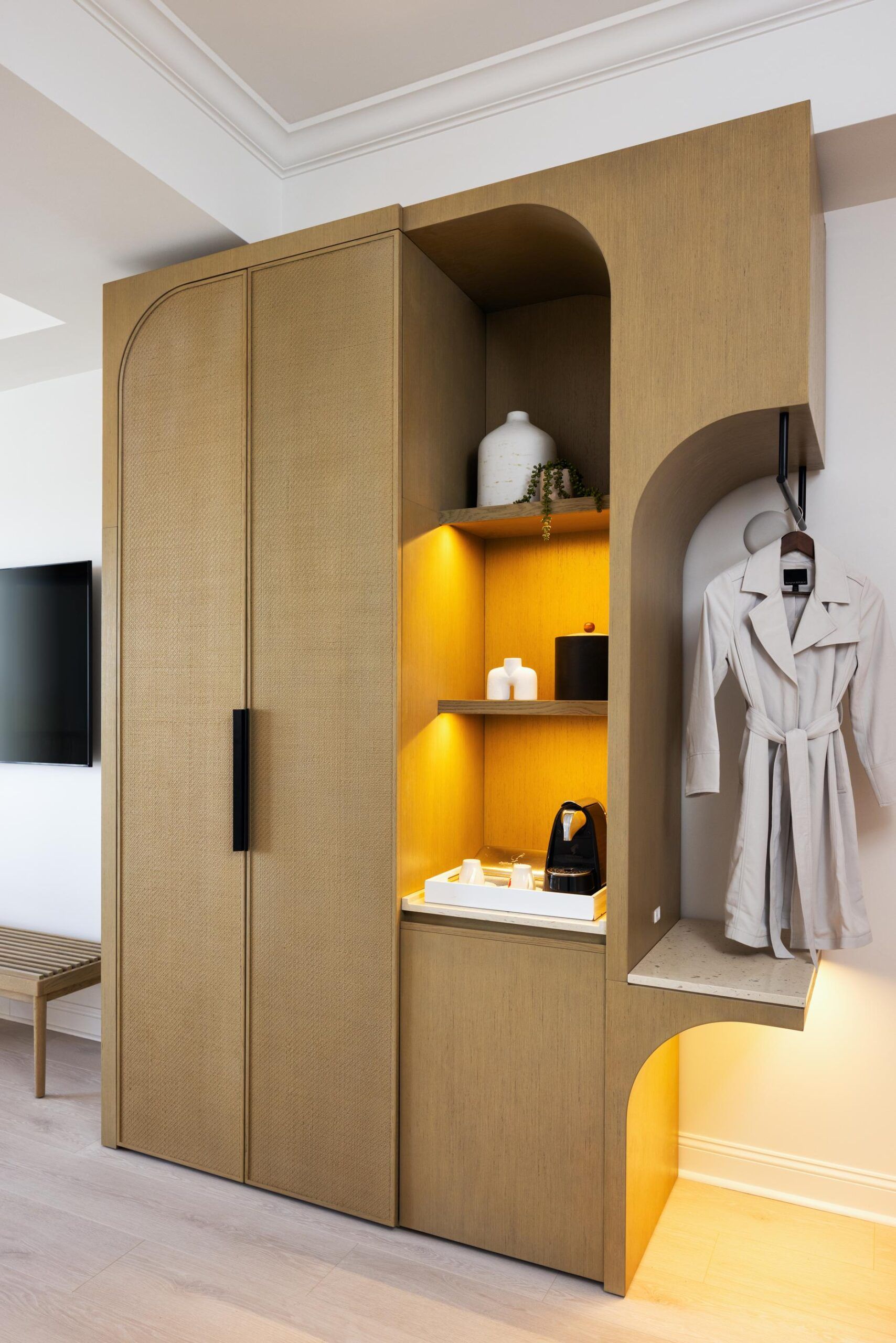 Wooden wardrobe with a small open shelf, lighted niches, and a white bathrobe hanging on the side, designed for accessibility.