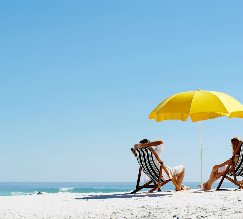 People sitting in lounge chairs under a yellow umbrella on the beach
