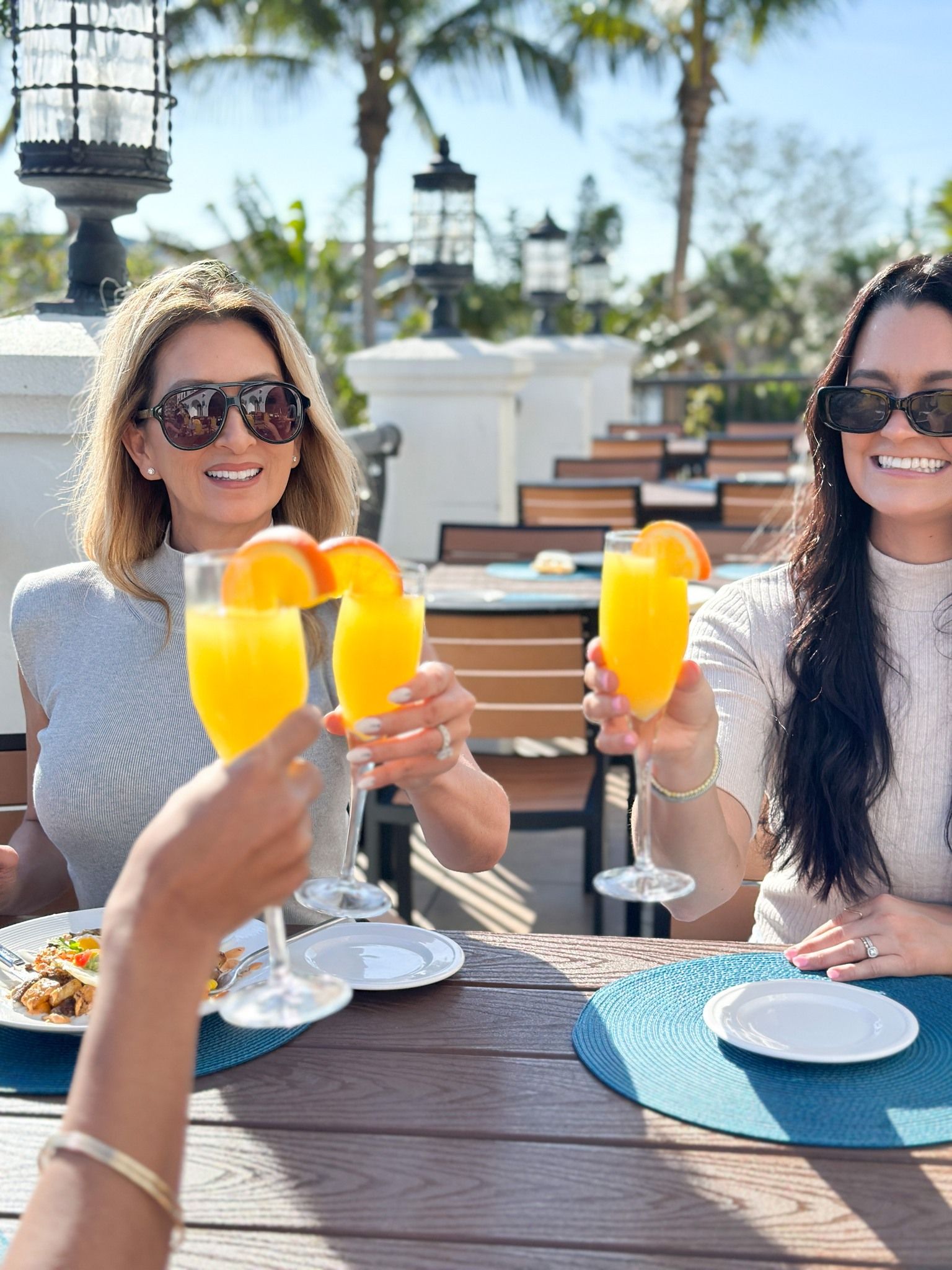 Three women sitting at a table outside smiling and doing a cheers with their drinks at Castile Restaurant in St Pete Beach